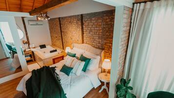 A bedroom with a brick wall, a bed with white bedding, a bedside table with a lamp, and a green chair.