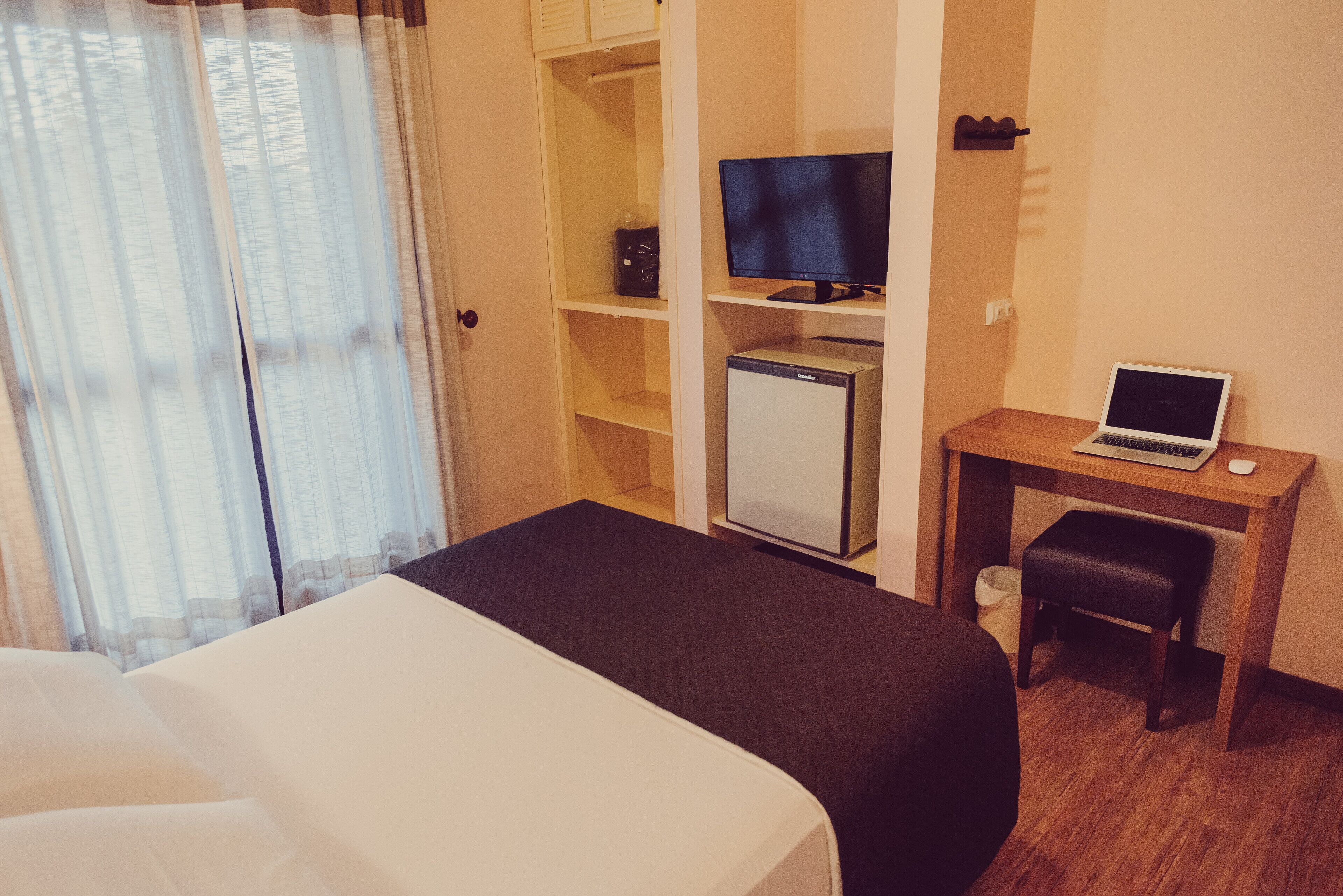 Habitación de hotel con cama, escritorio con computadora portátil, televisión y refrigerador pequeño.