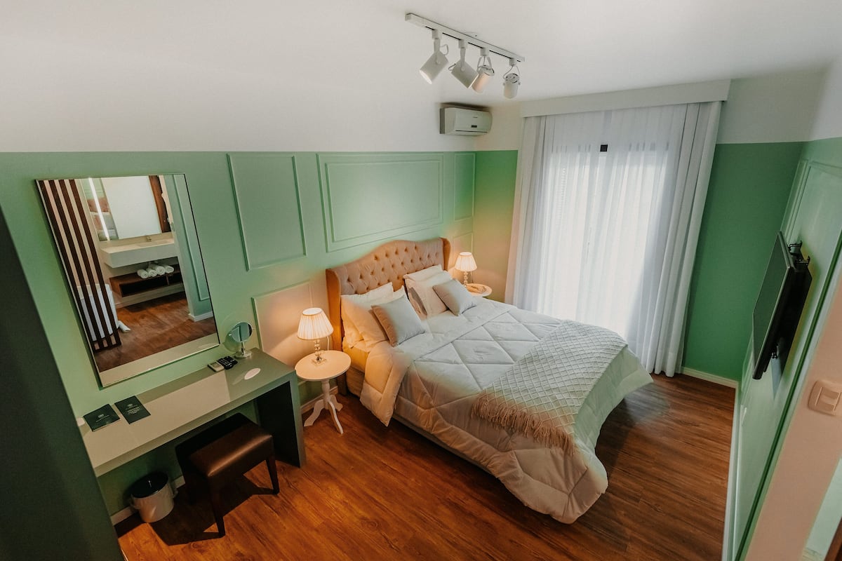 Un dormitorio con cama, mesitas de noche, un escritorio, un espejo y una ventana con cortinas.