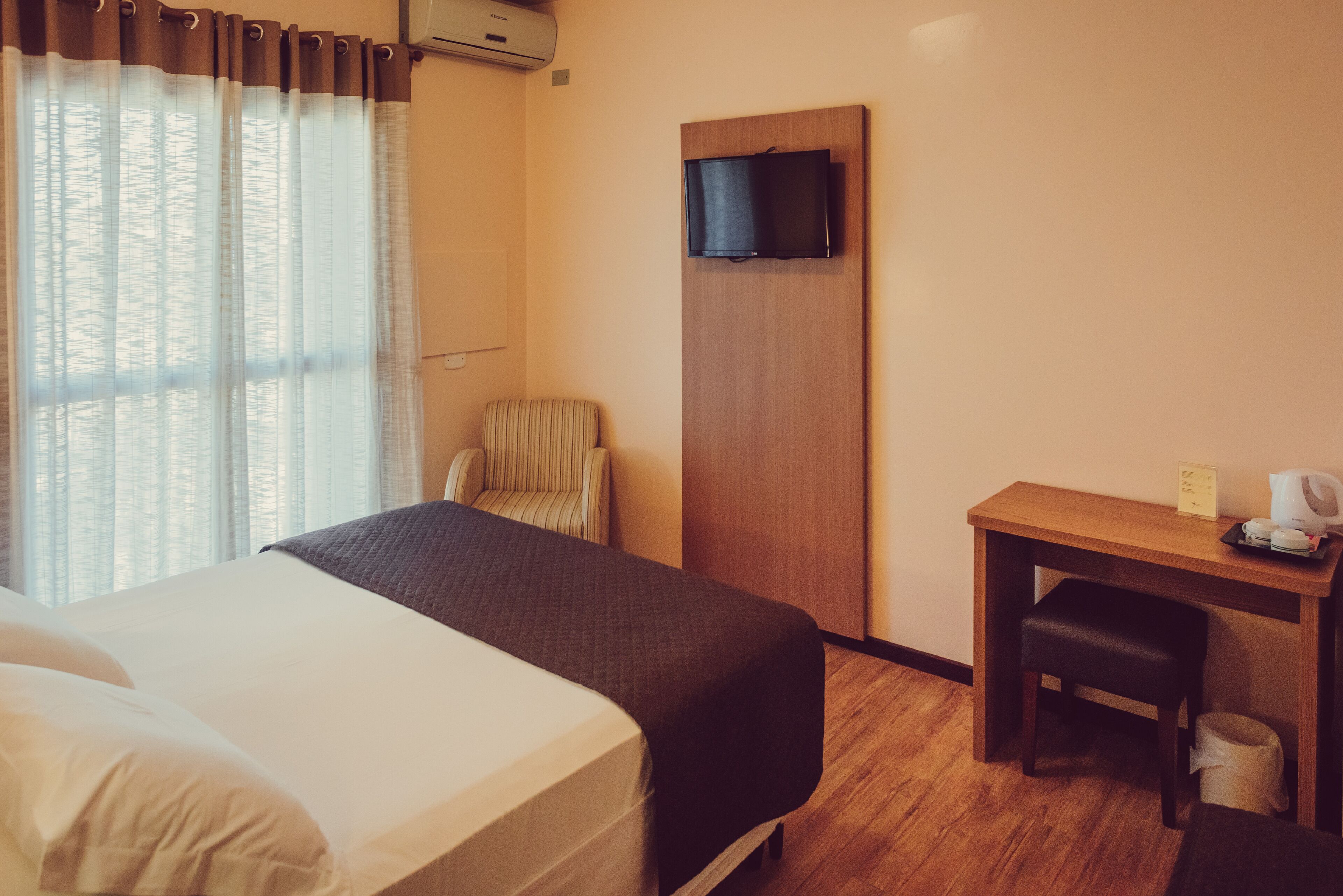 Habitación de hotel con cama, escritorio, silla, televisor y ventana con cortinas.