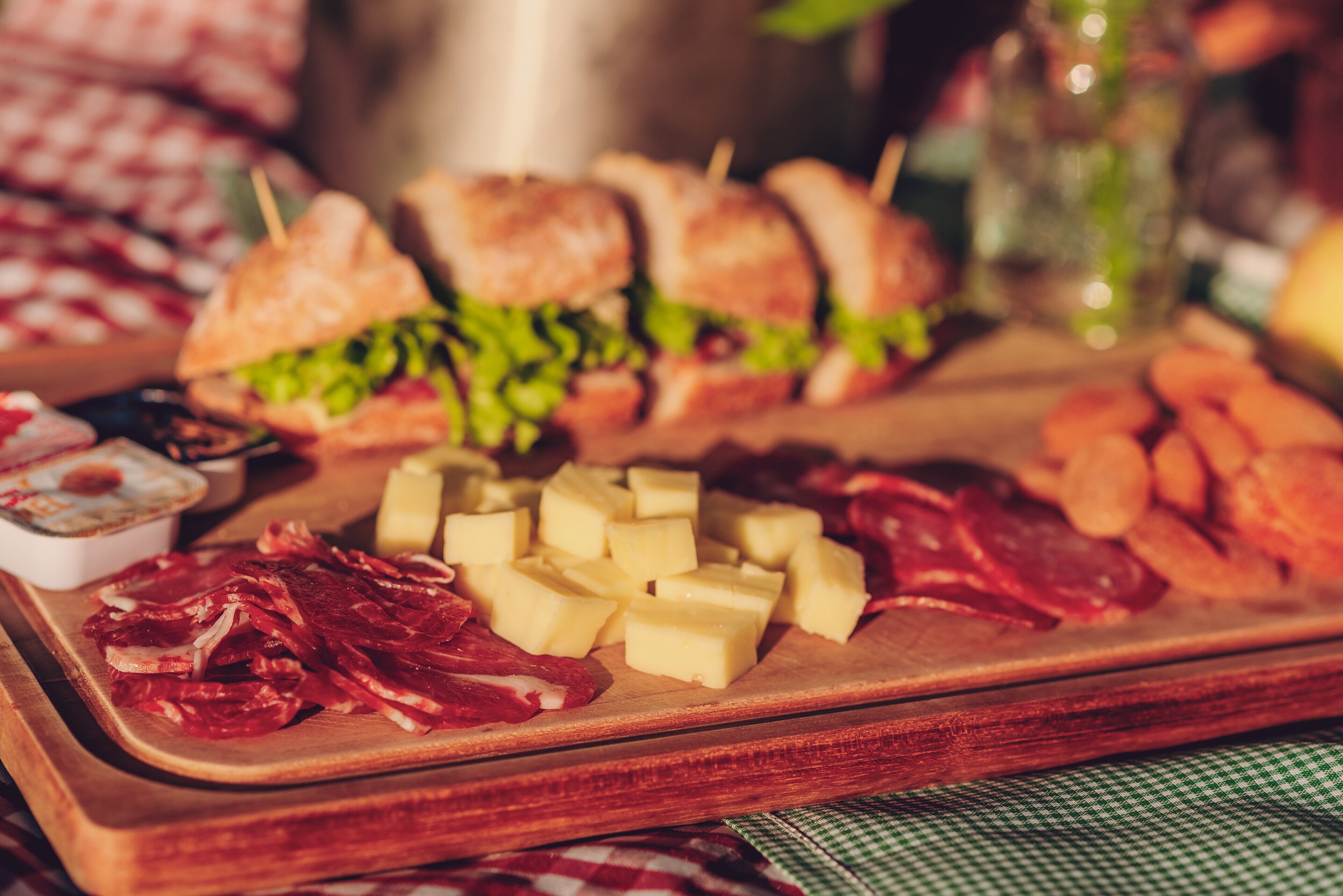 Una tabla de madera con diversos alimentos, como sándwiches, queso y embutidos.