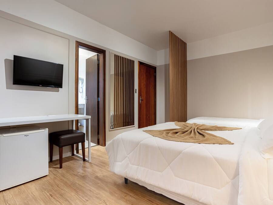 Habitación de hotel con cama, televisión montada en la pared, refrigerador pequeño y puerta de madera.