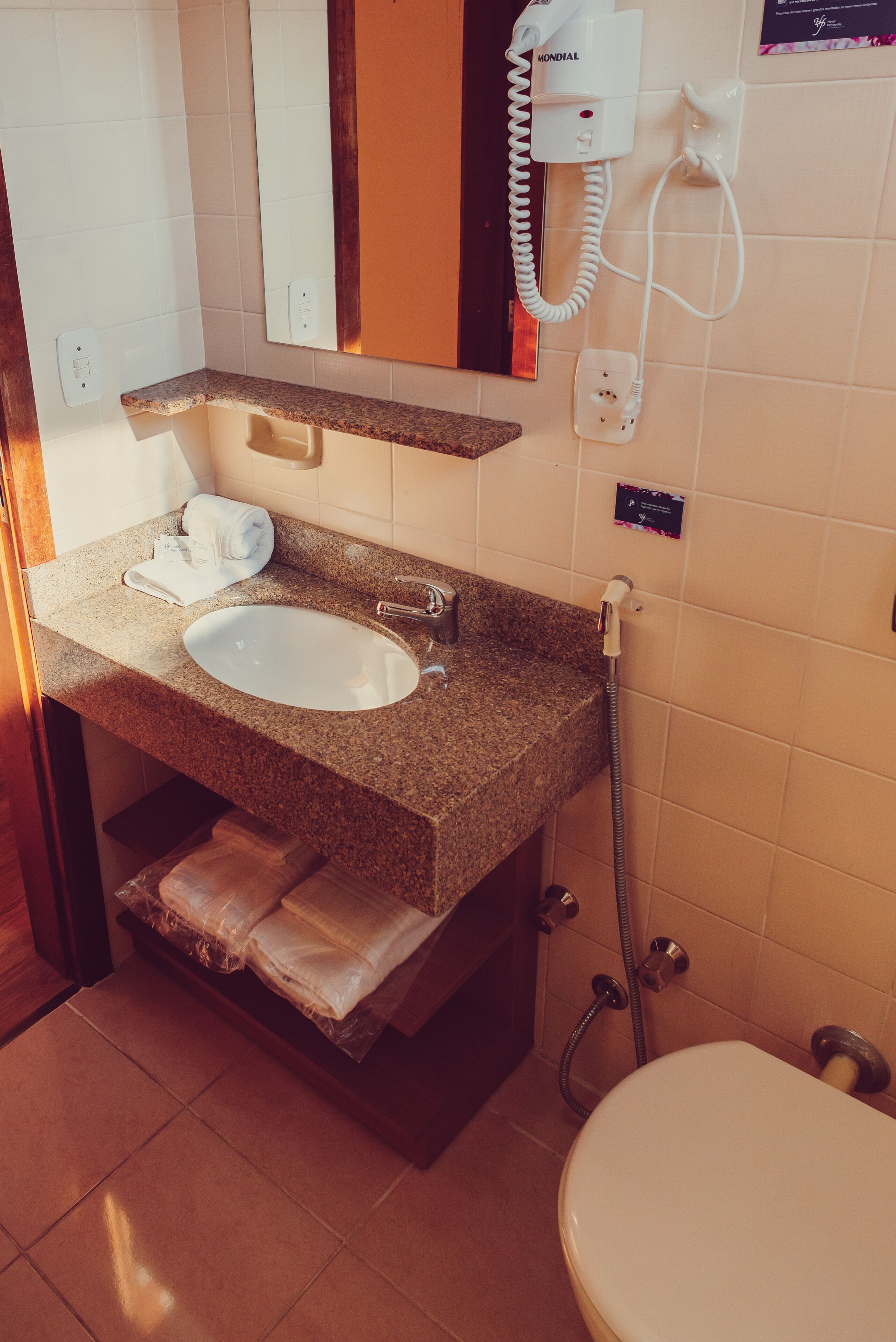 Un baño con lavamanos de encimera de granito, un espejo, un secador de pelo y un inodoro.