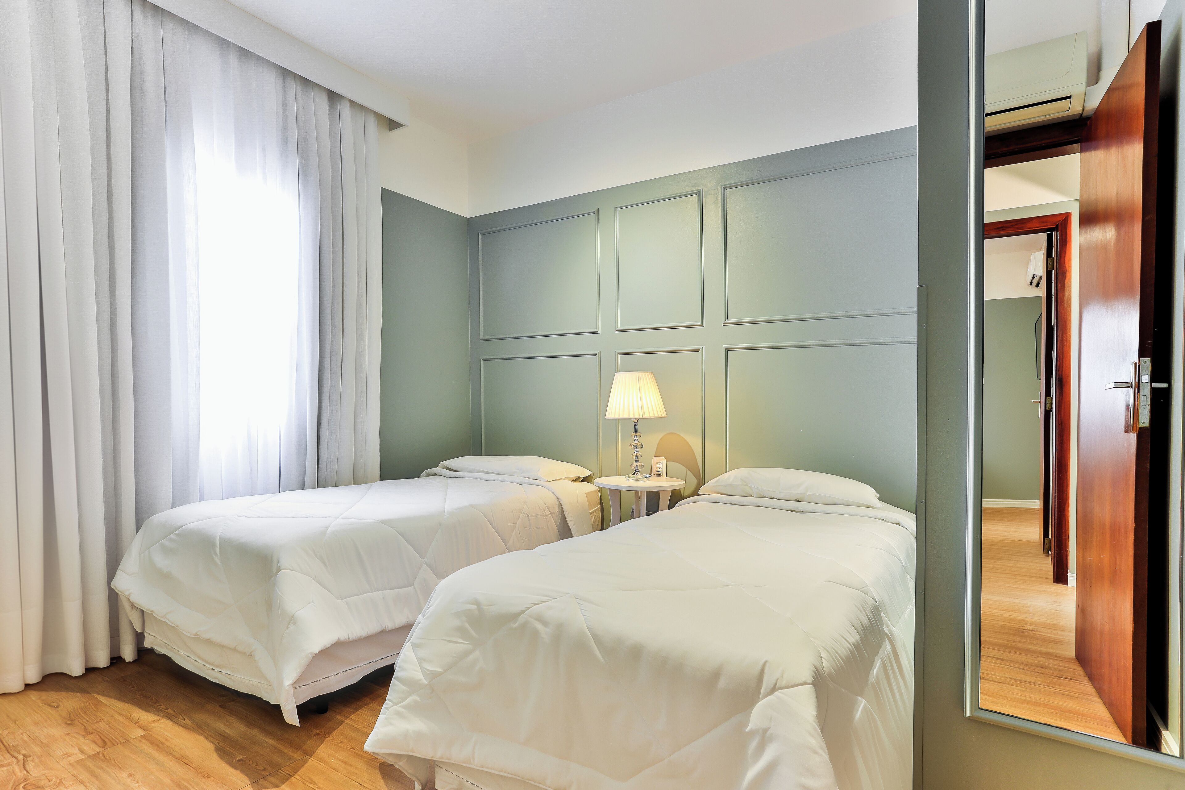 A hotel room with two beds, a small table with a lamp, and a mirror.