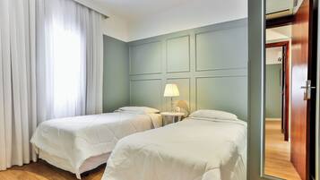 A hotel room with two beds, a small table with a lamp, and a mirror.
