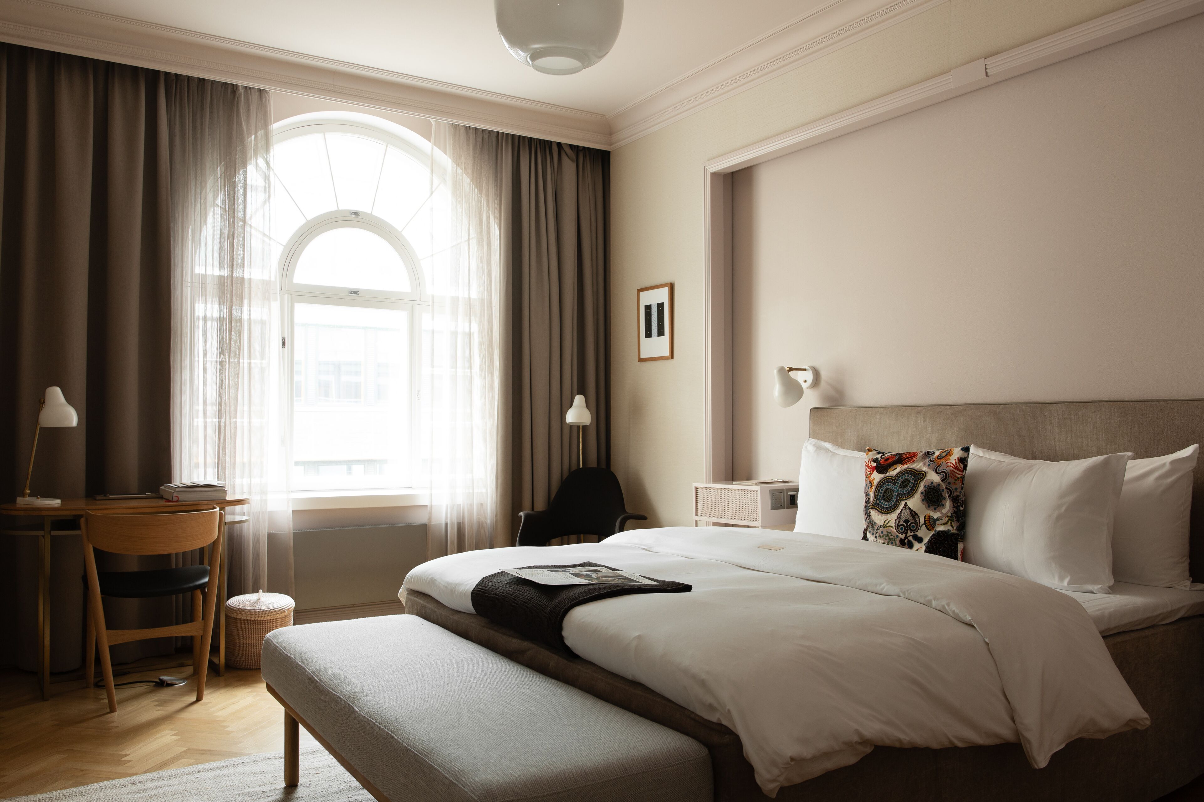 A hotel room with a large bed, a desk, a chair, and a window with curtains.