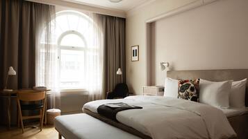 A hotel room with a large bed, a desk, a chair, and a window with curtains.