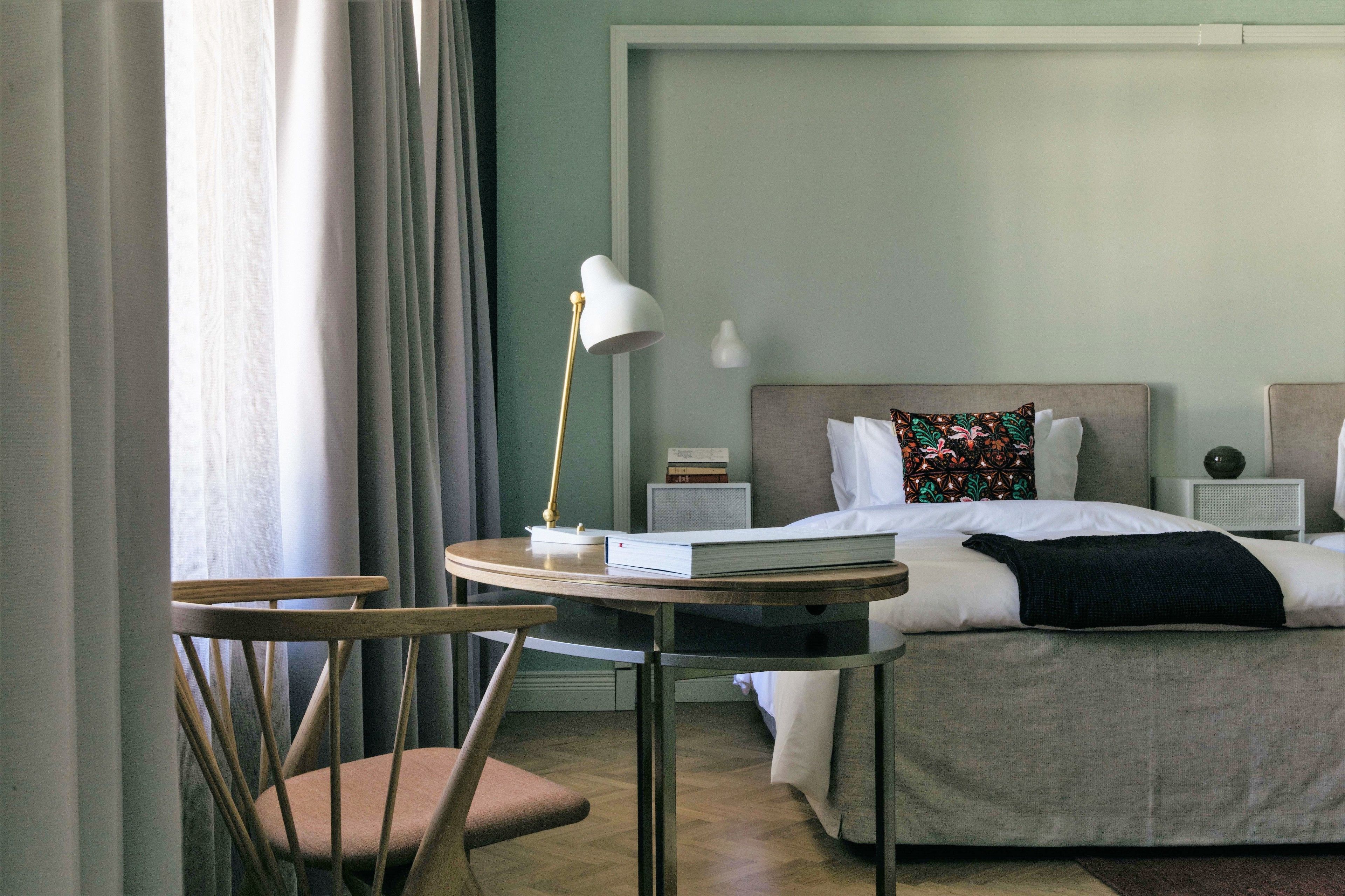 A hotel room with a bed, bedside tables, a lamp, a chair, and a table with a book.