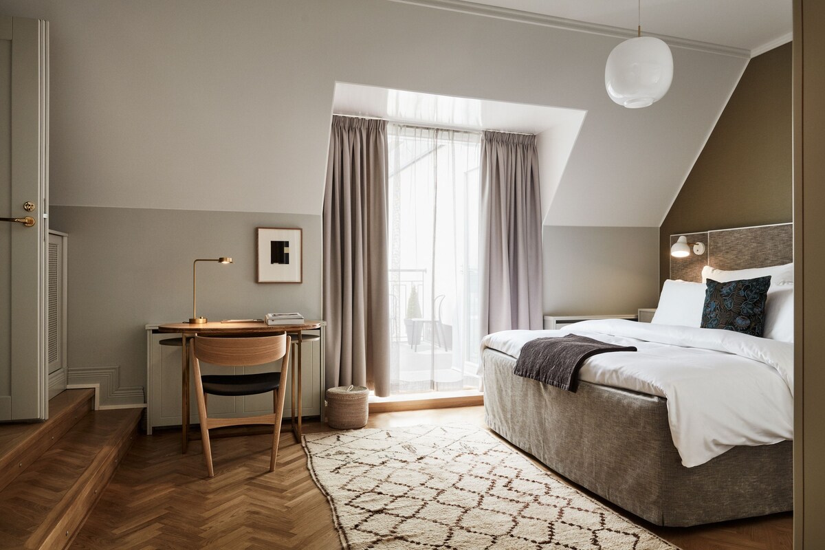 Une chambre à coucher avec un lit, un bureau, une chaise et une fenêtre avec des rideaux.