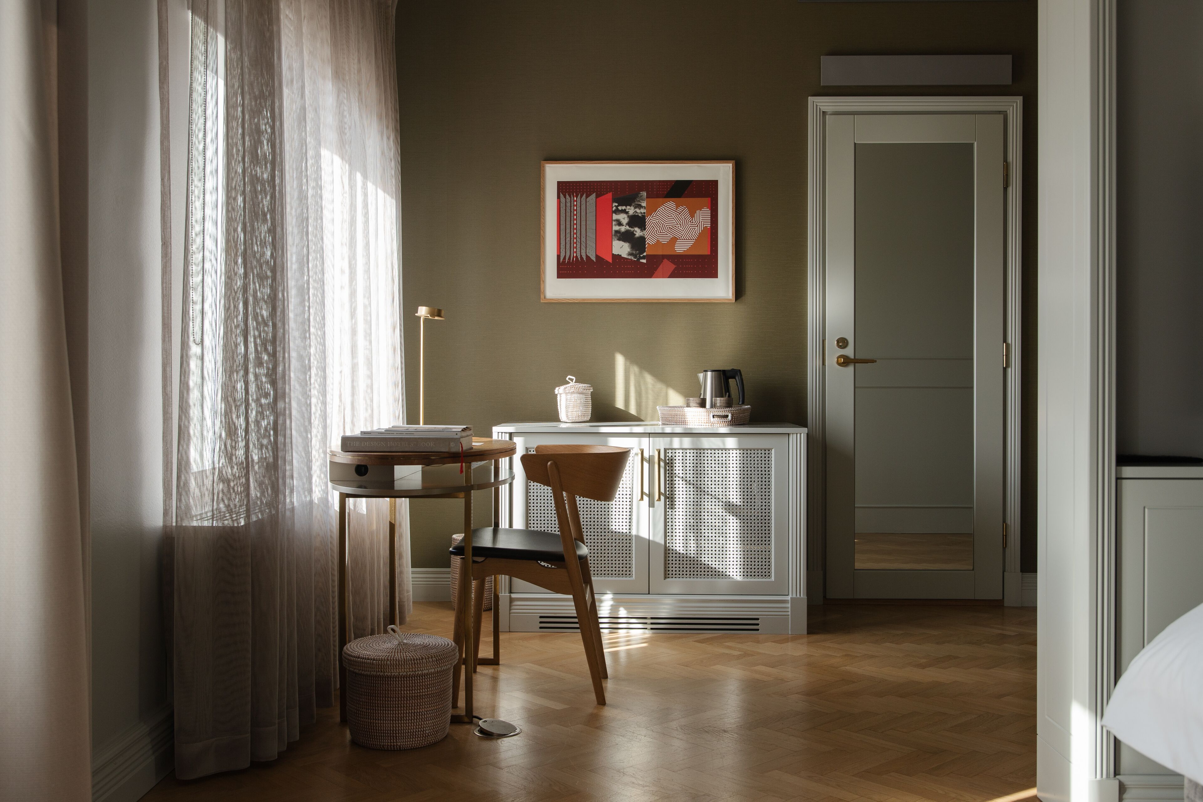 A room with a wooden floor, a chair, a table, a cabinet, a door, and a framed picture on the wall.