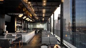 A modern bar area with a long counter, bar stools, and a seating area with sofas and a fire feature.
