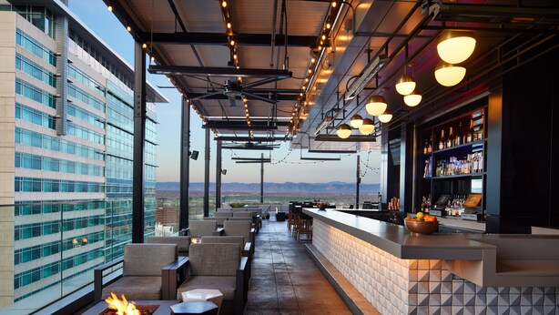 A rooftop bar with outdoor seating, a bar counter, and a fire feature.