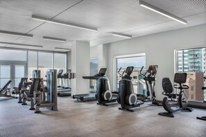 A modern gym with various exercise machines, large windows, and a view of the cityscape.