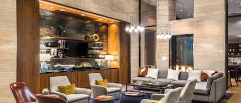 A modern living room with a sofa set, armchairs, and a coffee table. There is a fireplace and a television on a wooden cabinet.