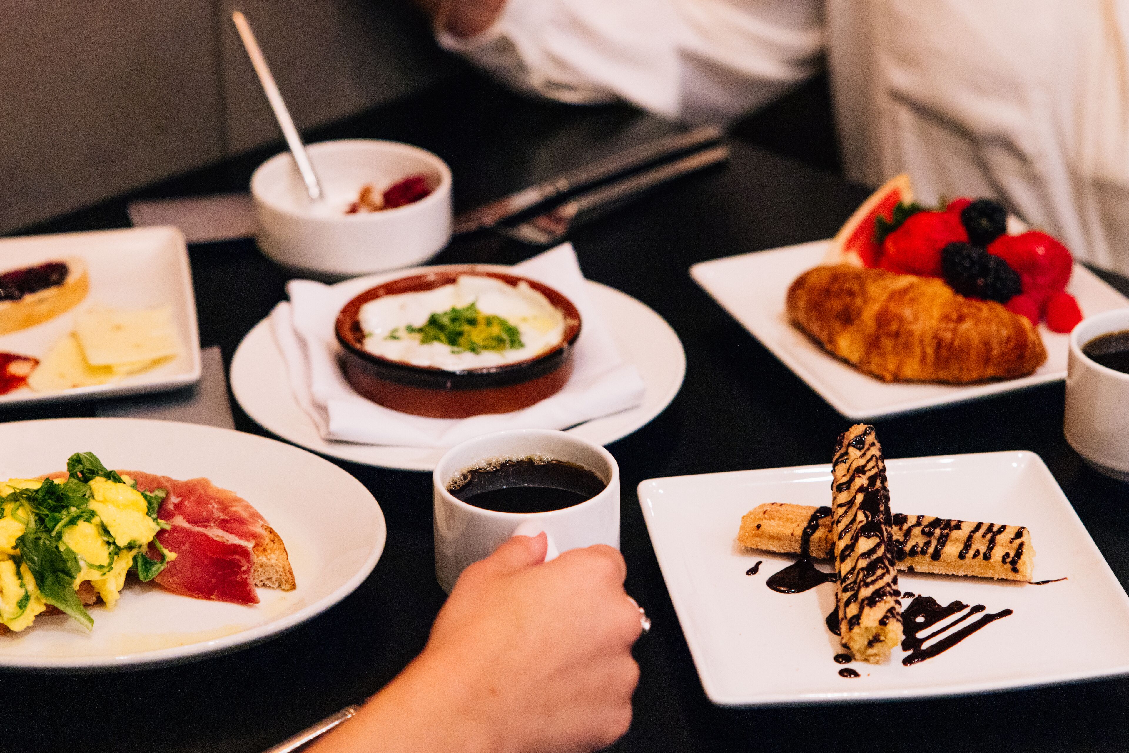 A variety of breakfast dishes on plates, including scrambled eggs, smoked salmon, and a croissant with chocolate drizzle.