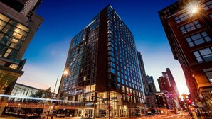 A modern hotel with a prominent glass facade, located at a city intersection with visible street traffic.