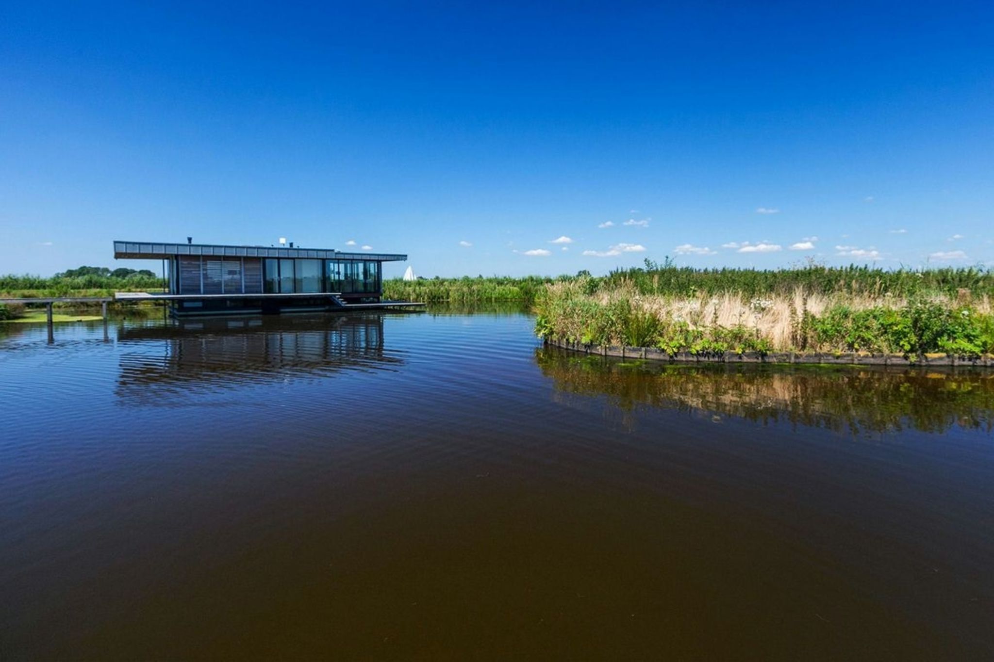 Una casa flotante moderna sobre un cuerpo de agua tranquilo con cielo despejado.