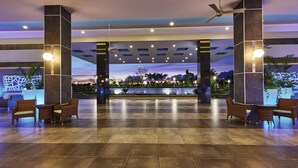 Un hall d’entrée spacieux offrant une vue sur un coucher de soleil se reflétant sur une étendue d’eau, et agrémenté de meubles modernes et de ventilateurs de plafond.