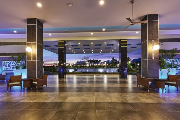 A spacious lobby with a view of a sunset over a body of water, featuring modern furniture and ceiling fans. - Hotel Riu Dunamar - All Inclusive (Costa Mujeres)