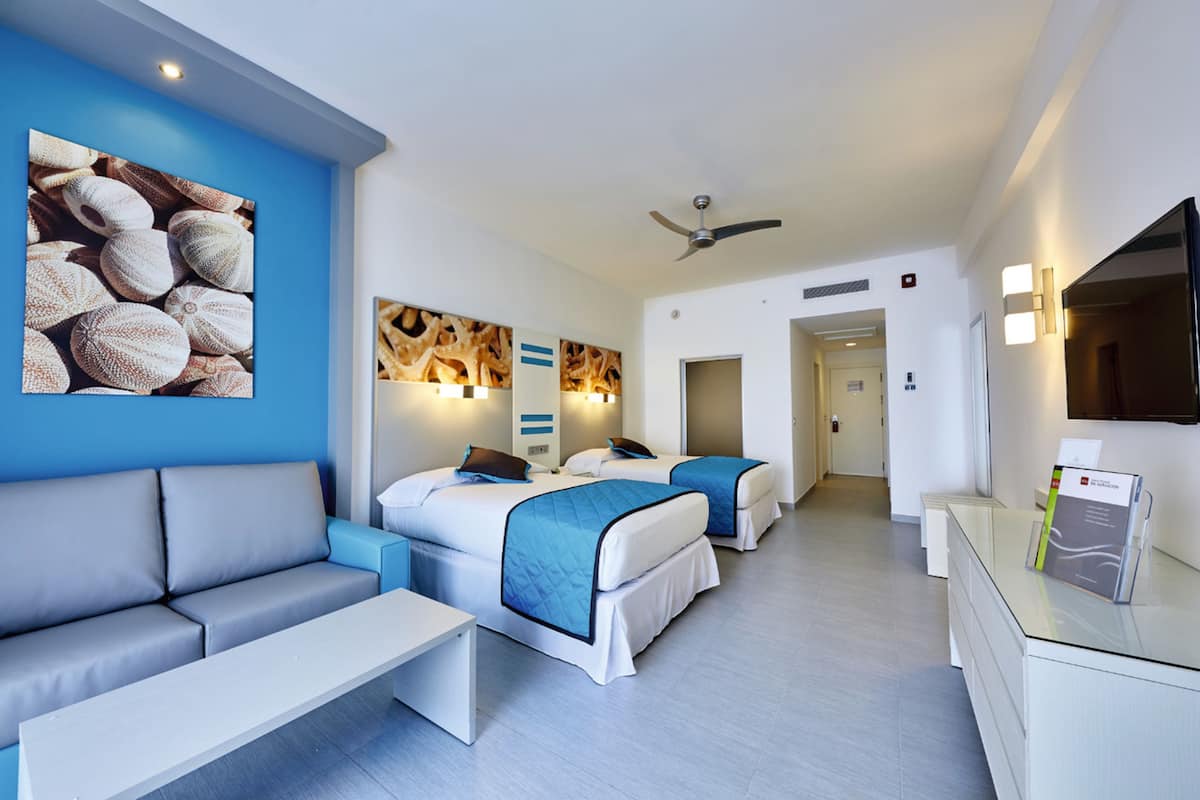 A hotel room with two beds, a sofa, a desk, and a TV.