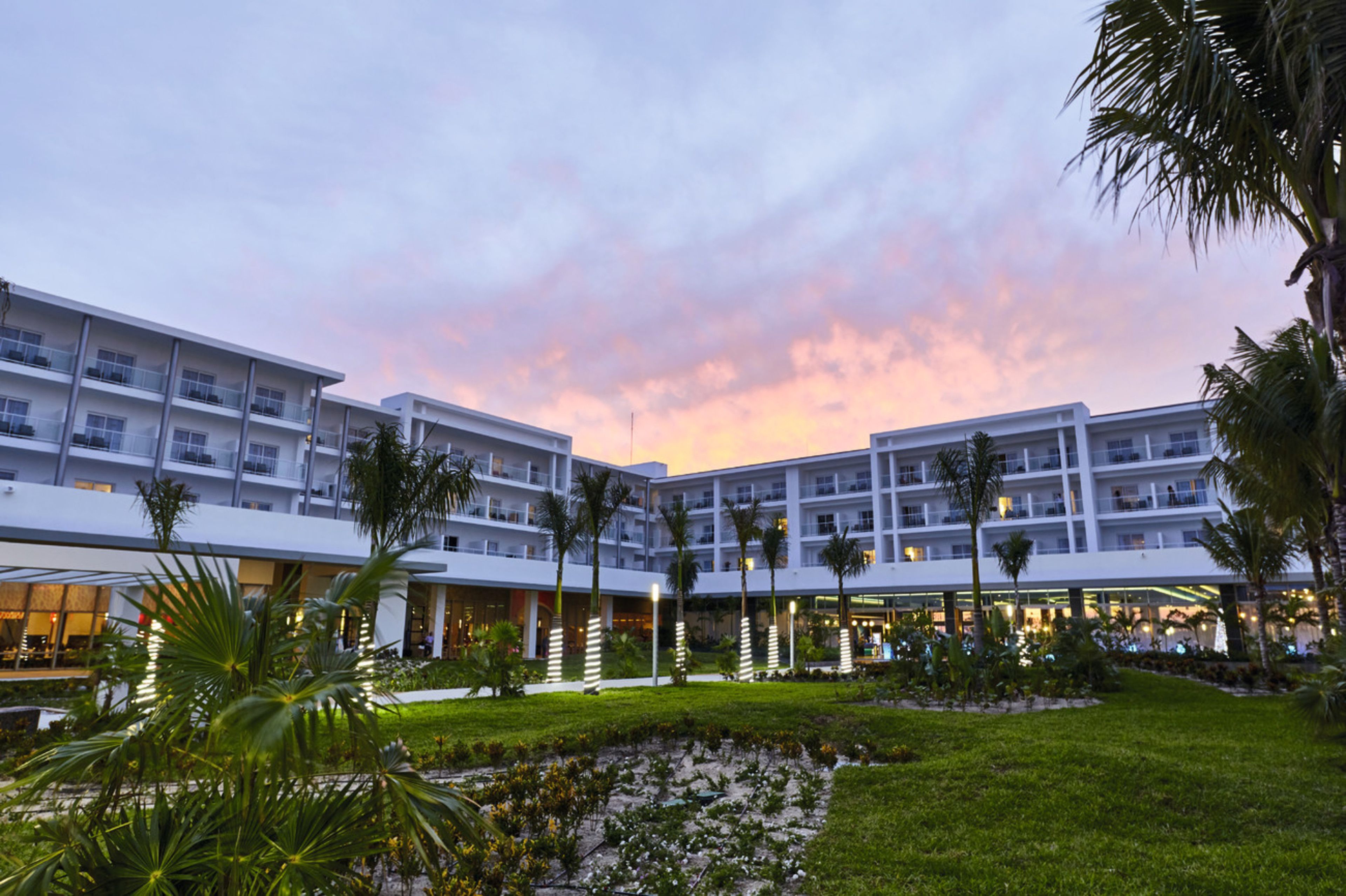 Un hôtel à étages, doté d’espaces extérieurs aménagés et de palmiers.
