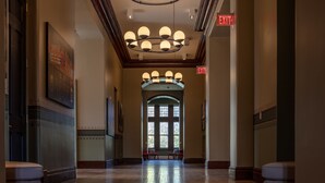 A hallway with a chandelier, an exit sign, and a large window at the end.