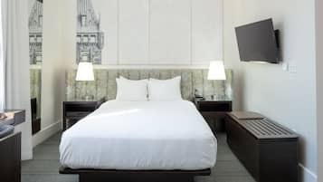 A hotel room with a large bed, two bedside tables with lamps, a flat-screen TV mounted on the wall, and a large window with a view of a building.
