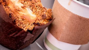 Un muffin en un vaso de papel marrón con un café en un vaso de papel blanco.