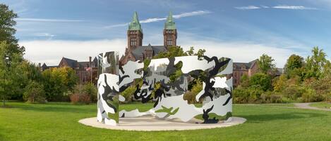 Une sculpture dans un parc, avec un bâtiment historique en arrière-plan.