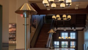 A spacious lobby with a long reception desk, multiple chandeliers, and a staircase leading to upper floors.