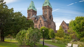 A historic building with two towers, surrounded by lush greenery and a pathway with benches.