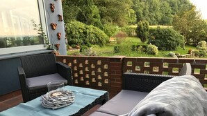 Un patio con mobiliario de mimbre, una mesa cubierta con un mantel azul y vista a un jardín.