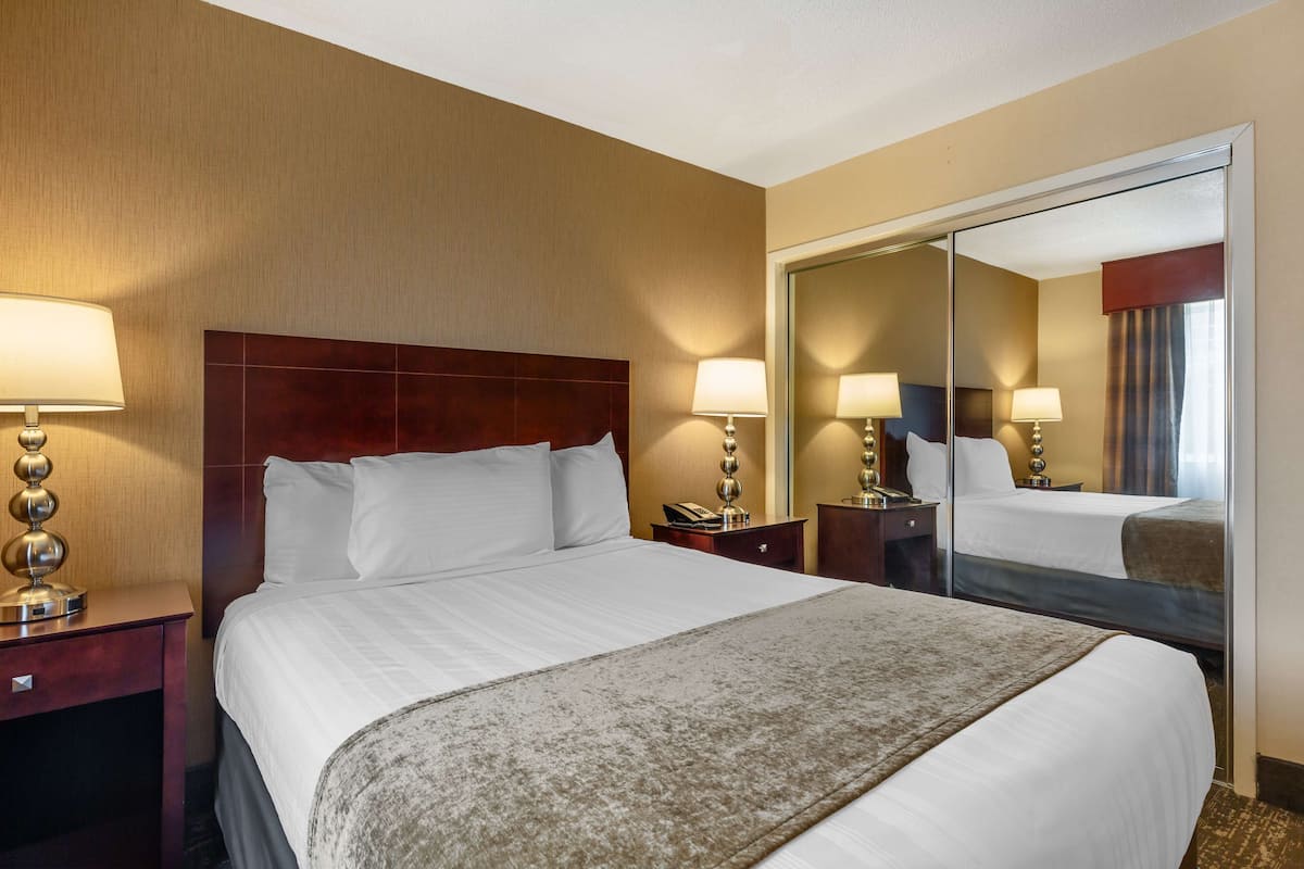 A hotel room with a large bed, two bedside tables, a mirror, and a nightstand.