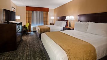 A hotel room with two beds, a desk with a television, a chair, and a lamp.