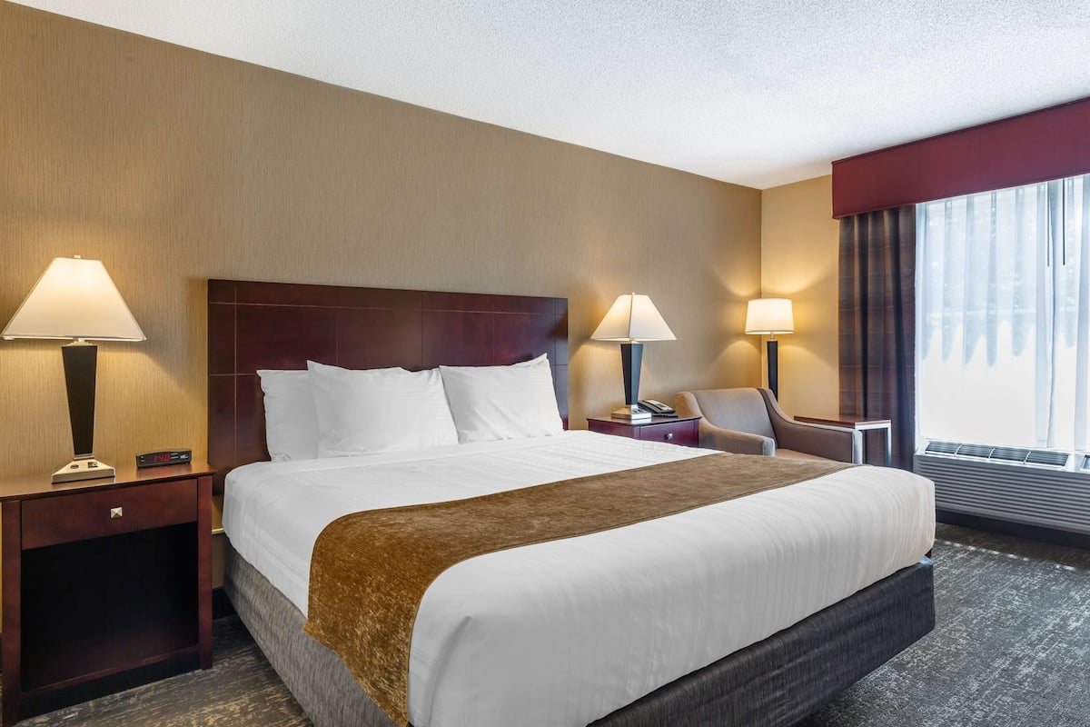 A hotel room with a large bed, two bedside tables with lamps, a chair, and a window with curtains.