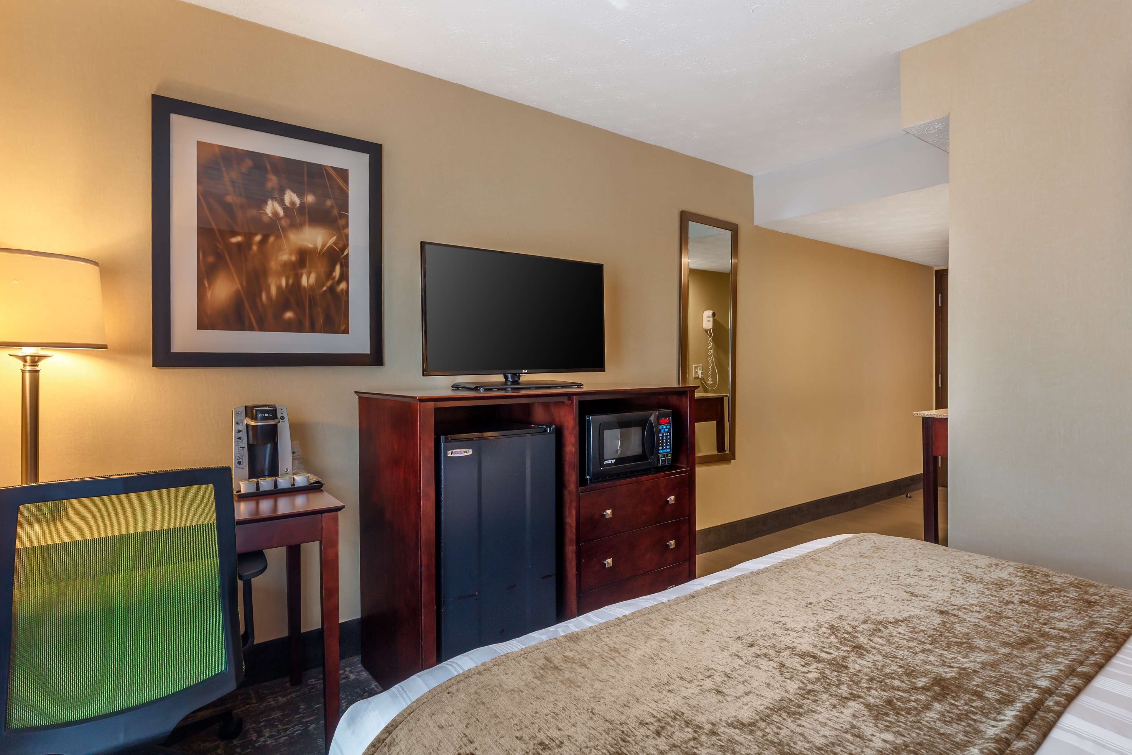 A hotel room with a bed, a desk with a computer, a television, a microwave, and a refrigerator.