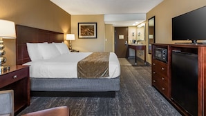 Una habitación de hotel con cama, mesita de noche, lámpara, cómoda, televisión y espejo.