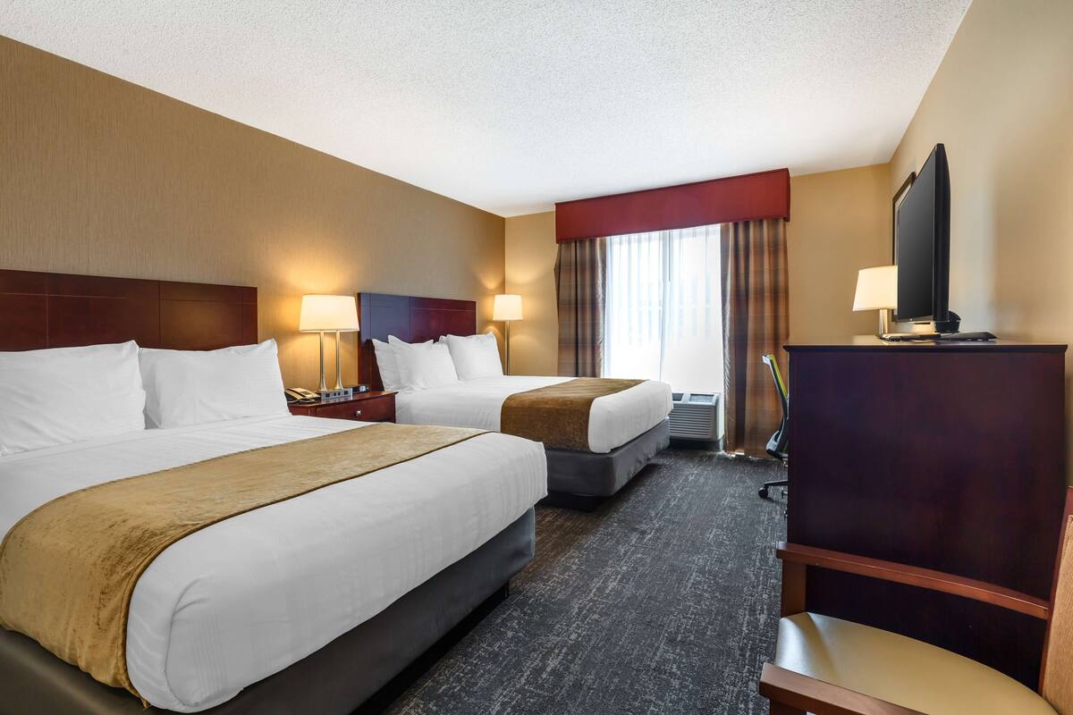 A hotel room with two beds, a TV, a desk, and a chair.