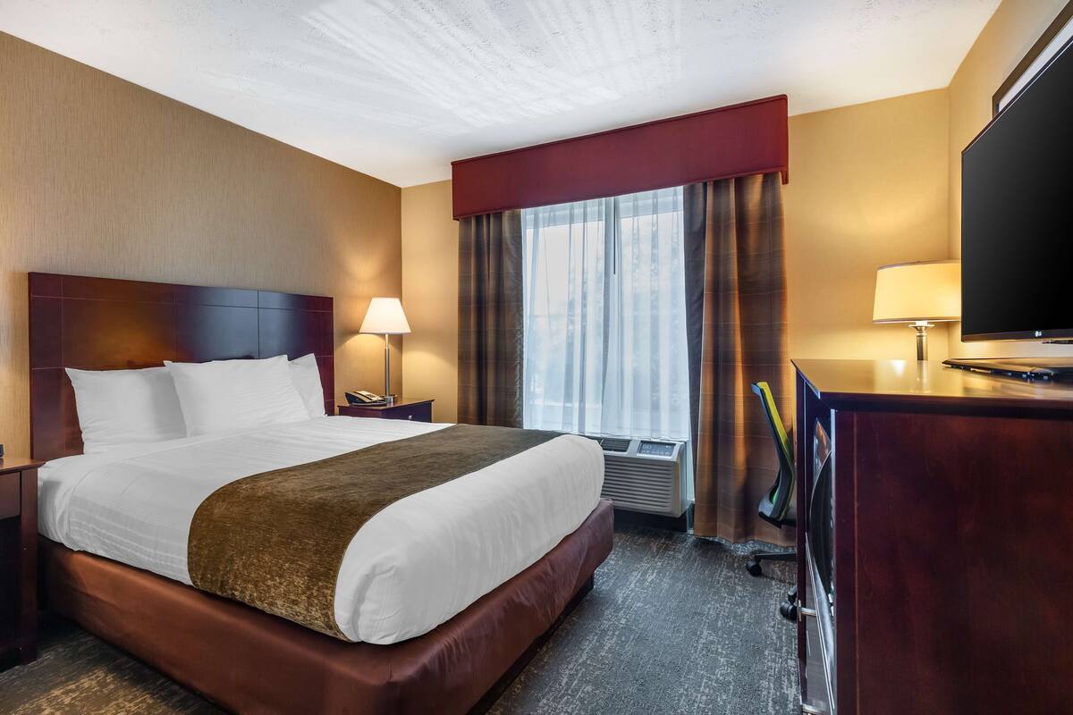 A hotel room with a large bed, a desk, a TV, and a window with curtains.
