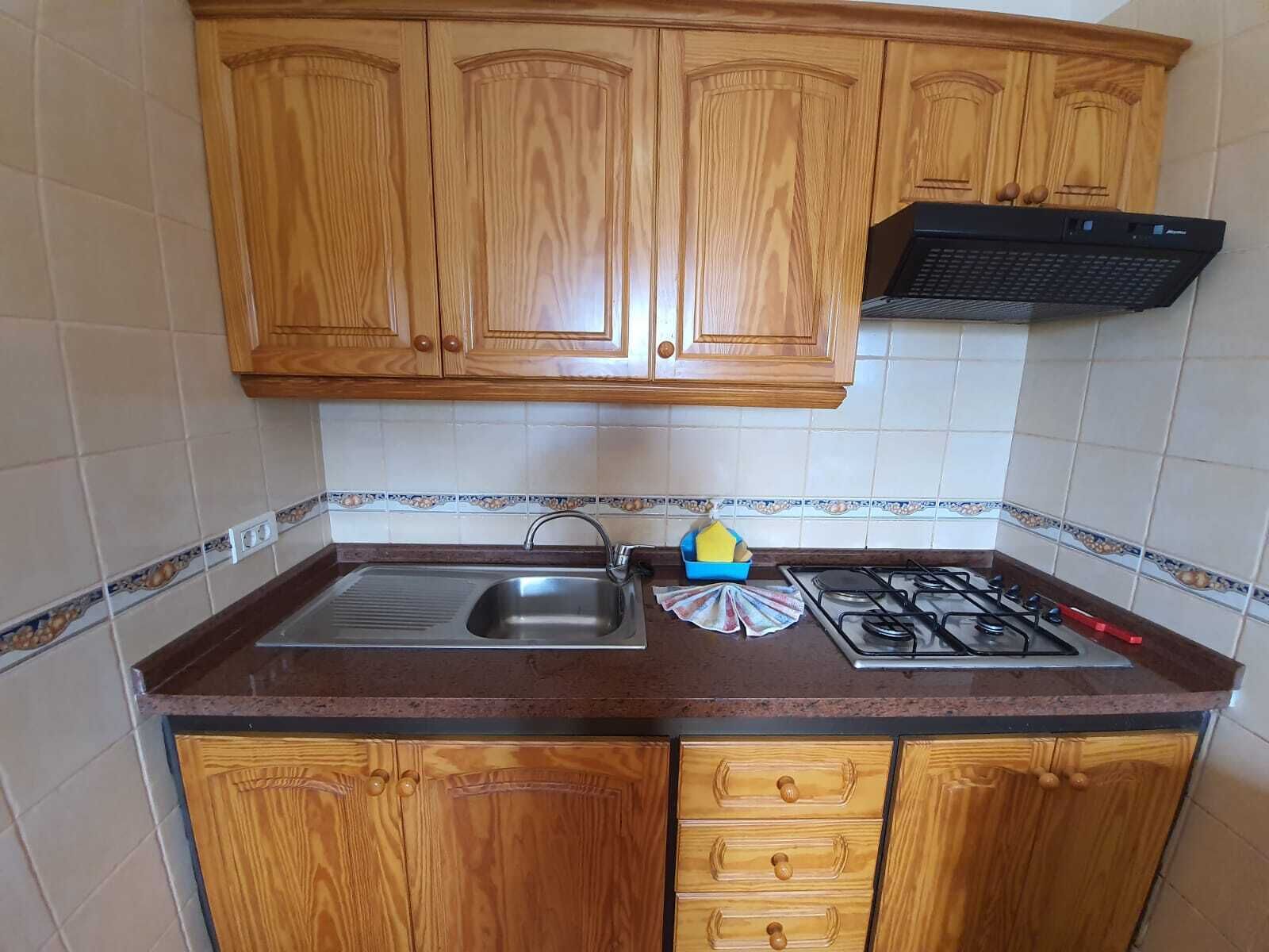 Une cuisine avec des meubles de rangement en bois, un évier en acier inoxydable, une cuisinière à gaz et un égouttoir bleu.