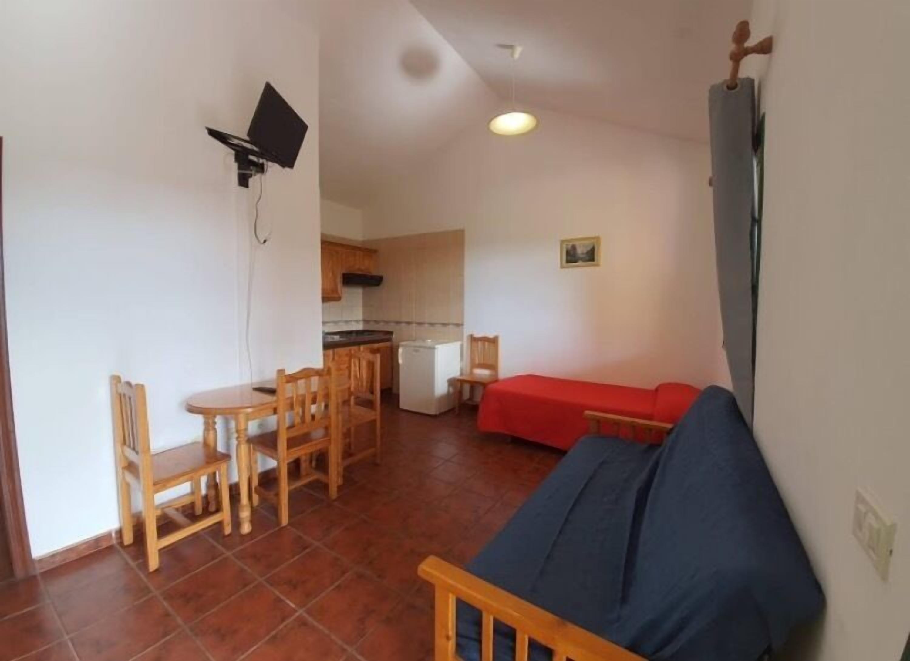 Un espacio habitable compacto con comedor, kitchenette y un sofá rojo.