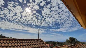 A rooftop with terracotta tiles and a clear sky with scattered clouds.