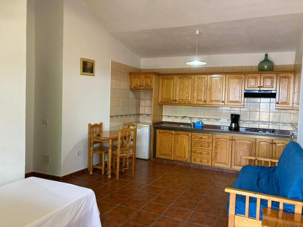 Uma cozinha compacta com armários de madeira, um espaço de refeições com mesa e cadeiras, e um pequeno sofá.