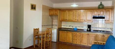 Uma cozinha compacta com armários de madeira, um espaço de refeições com mesa e cadeiras, e um pequeno sofá.