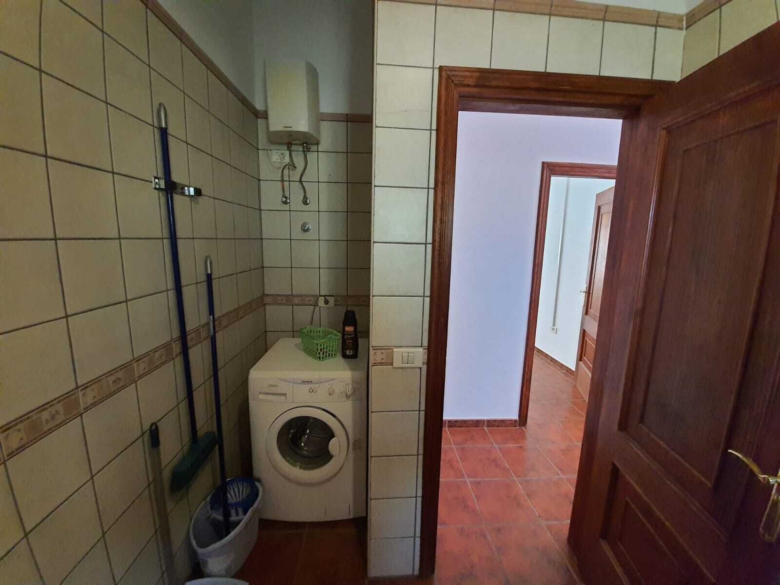 A compact bathroom with a washing machine, a mop, and a bucket.