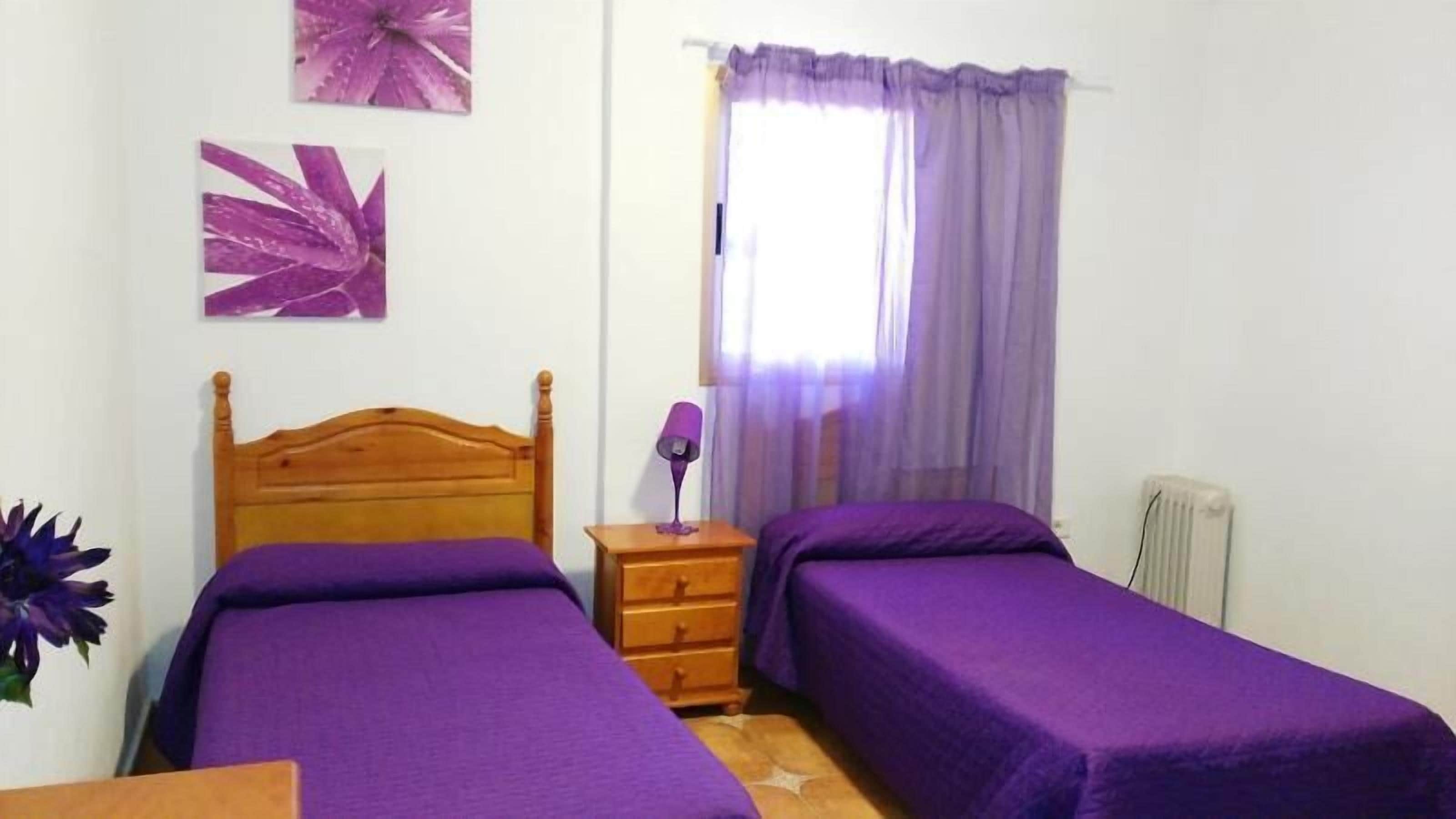 A bedroom with two single beds, a wooden headboard, a nightstand with a lamp, and a radiator.