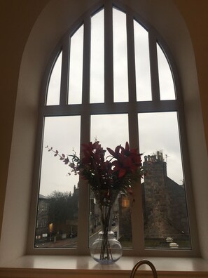 A window with a vase of flowers, a view of a historic building, and a clear sky.