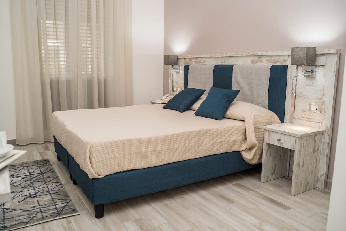 Un llit amb capçalera, taules de nit i una finestra amb cortines.