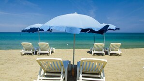 Una playa con sillas de descanso blancas y sombrillas azules.