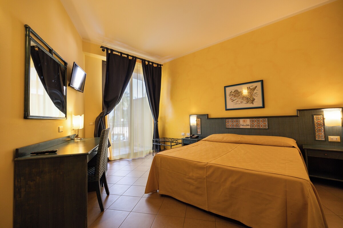 A hotel room with a bed, a desk, a chair, a TV, and a window with curtains.